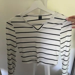 Vit och svart randig tröja - Säljer en croppad långärmad tröja från Shein i storlek S. Tröjan är vit med svarta ränder, har ribbad struktur och en liten v-ringad detalj vid halsen. Perfekt för dig som gillar enkel och stilren look.