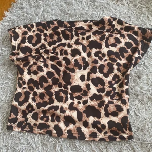 Leopardmönstrad croppad topp - Snygg croppad topp med leopardmönster i brunt och beige. Toppen har korta ärmar och en öppen rygg som ger en cool vibe. Tillverkad i stretchigt syntetmaterial som sitter tight och framhäver figuren. Perfekt för dig som vill sticka ut med ett djurmönster. Använd endast en gång!!