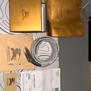 Burberry bälte med rutigt mönster - Säljer ett Burberry bälte med ikoniskt rutigt mönster och metallspänne med Burberry-logga. Finns i två färger: klassisk beige med röda och bruna rutor samt helsvart med diskret rutmönster. Bältet är tillverkat i skinn och levereras med originalförpackning och certifikat.