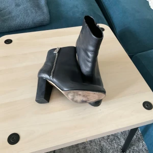 Svarta skinnstövletter med klack - Snygga svarta stövletter i skinn med rund tå och kraftig hög klack. Dragkedja på sidan i silver ger en cool detalj. Perfekta till både jeans och kjol för en stilren look.