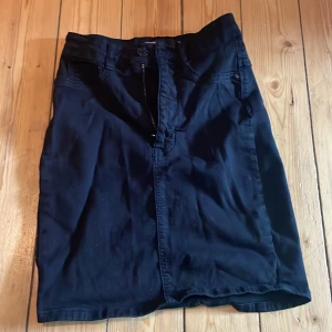 Svart jeanskjol från ginatricot  - Svart jeanskjol från ginatricot , modell Molly. Kjolen har klassisk femficksdesign, knapp och dragkedja framtill samt bakfickor. Rak passform och knälång (slutar över knä) stil som funkar till sneakers eller boots. Perfekt för dig som gillar enkel och clean look.