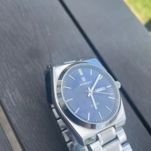  Poedagar klocka  - Stilren klocka från Poedagar med blå urtavla och dag/datumvisning. Boetten och länken är i blankt silverfärgat metall, och designen är klassisk med minimalistiska index. Perfekt accessoar för dig som gillar en clean look.