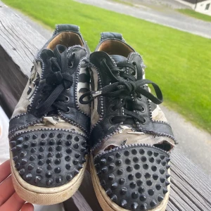 Christian Louboutin sneakers med nitar - Unika sneakers från Christian Louboutin med svartvita zebramönster, svarta nitar på tån och klassisk röd sula. Skorna har svarta snören, kontrastsömmar och detaljer i skinn. Perfekt för dig som vill sticka ut med edgy streetstyle. Skriv vid fundering 