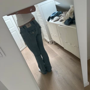 Blå bootcut jeans från True Religon - På sista bild ser man att jeansen har ett hål, men det är nått som säkert gå att laga, Snygga ljusblå jeans från true religon med bootcut passform och lågmidjade. Klassiska fickor med lock och knapp bak. Jeansen har en låg midja och är tillverkade i mjukt denim. Perfekta för dig som gillar en retro vibe och vill ha ett par jeans som sticker ut.