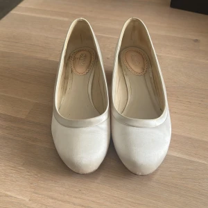 Vita pumps med låg klack i satin - Stilrena vita pumps från Pink med rund tå och låg klack. Skorna är tillverkade i satin som ger en elegant känsla. Perfekta för dig som vill ha en klassisk och enkel sko med feminin touch. Storlek 38