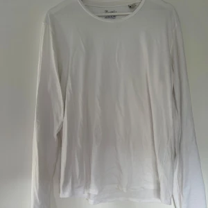 Vit långärmad tröja Scotch & Soda - Klassisk vit långärmad tröja från Scotch & Soda i 100% bomull. Enkel och stilren design med rund halsringning och diskret metallogo vid nederkanten. Perfekt för dig som gillar en clean och avslappnad look.