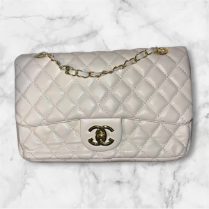 Chanel quiltad axelväska i skinn - Supersnygg quiltad axelväska från Chanel i ljusbeige skinn med klassiskt CC-spänne i guld och kedjerem. Väskan har ett tidlöst rutmönster och innerfack, perfekt för att lyfta vilken outfit som helst. Ikonisk design som aldrig går ur tiden.