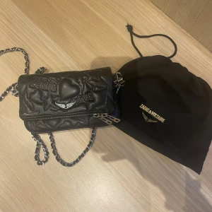Zadig voltaire väska - Äkta Zadig väska, köpt i en Zadig voltaire butik i Paris. Använd många ggr men fortfarande super fint skick. Den har en blå söm + blåa diamanter. Olika ord på den som tex ”zadig”, ”love”, ”voltaire”,”amour”. Kommer med dustbag!
