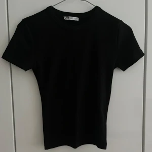 Svart kroppad t-skjorta - En svart kroppad t-skjorta från Zara. Materialen är strechigt och sitter snyggt på kroppen. Perfekt för flera tillfällen. 🩷🩷