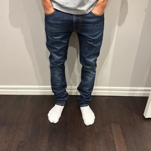 Mörkblå jeans från Nudie Jeans, 29/32 - Säljer ett par mörkblå jeans från Nudie Jeans med klassiska orange sömmar och snygga detaljer på bakfickorna. Modellen har en slim passform och är perfekta för en lite avslappnad stil. Nypris är 1600 men vårt pris är 799 men de går att diskuteras. Skriv med mer frågor.