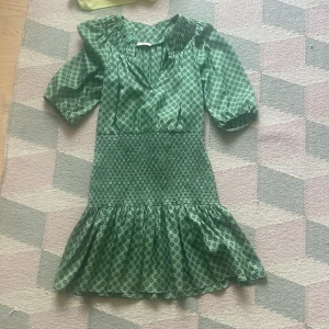 Grön Sandro klänning - Säljer en grön kortklänning med prickigt mönster och volang nedtill. Klänningen har puffiga kortärmar, v-ringad hals och smockad midja. Strl 36 i princip nyskick❤️