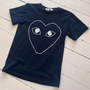  CDG Comme des Garçons T-shirt  - Mörkblå  t-shirt från Comme des Garçons med stort vitt hjärta och ögon på bröstet. Klassisk rund hals och korta ärmar. Perfekt för dig som gillar statement-plagg och vill sticka ut med en unik design. 🤩passar S/M