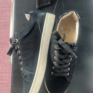 Svarta sneakers i mocka från Dasia - Snygga svarta sneakers från Dasia i mjuk mocka med vita sulor och svarta snören. Skorna har guldfärgade öljetter och en klassisk rund tå. Insidan är ljusbeige och bakkappan har en glansig detalj. Perfekta för en stilren och trendig look.