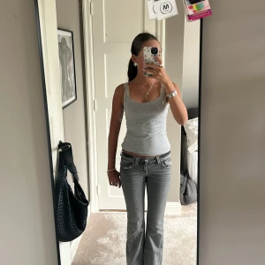 Grå bootcut jeans med låg midja - Säljer ett par grå jeans med bootcut och låg midja. Jeansen har klassiska fem fickor, snygga detaljer på bakfickorna och en lite utsvängd passform nertill. Säljer även för att dom är försmå!💕