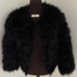 Svart fluffig pälsjacka - Säljer en svart pälsjacka från DM superfluffig look och lång ärm. Jackan har en kortare, boxig passform och är perfekt för dig som vill sticka ut med en statement-piece. Materialet är fjäder som ger en lyxig känsla och cool vibe.