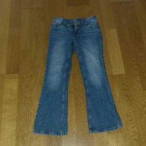 Blå bootcut jeans i storlek 158 - Snygga blå jeans med bootcut passform från Cubus i storlek 158. Klassisk femficksmodell med knappar på bakfickorna och bälteshällor. Jeansen har en lätt tvättad look och är tillverkade i mjukt denimtyg som sitter skönt hela dagen.