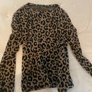 Leopardmönstrad långärmad tröja - Snygg långärmad tröja med leopardmönster i beige och svart. Tröjan har en rund halsringning och är i ett mjukt, stretchigt material som sitter skönt på kroppen. Perfekt för dig som vill sticka ut med ett djuriskt print.