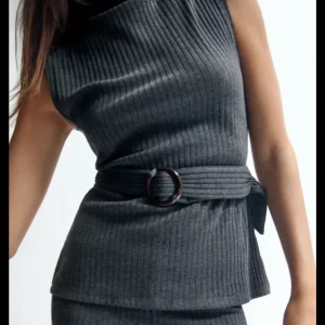 Grå ribbad topp med bälte - Snygg mörkgrå ribbad topp med bred midjebälte och rund spänne. Perfekt för dig som gillar minimalistisk look och vill ha något som sticker ut med coola detaljer.