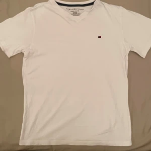 Tommy Hilfiger T-shirt  - Vit t-shirt från Tommy Hilfiger med klassisk v-ringning och liten broderad logga på bröstet. Enkel och stilren design, köpt i New York unik modell 