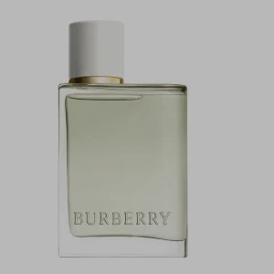 Burberry parfym med vit kork - Stilren parfym från Burberry i en transparent glasflaska med ljusgrön vätska. Flaskan har en vit, rund kork och en elegant gulddetalj vid halsen. Burberry-loggan är ingraverad framtill på flaskan.