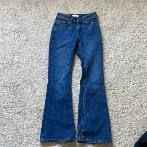 Blå bootcut jeans från Lindex - Snygga blå jeans från Lindex med klassisk bootcut-modell och fem fickor. Jeansen har normal passform och är tillverkade i mjukt denimtyg med kontrastsömmar. Perfekta för dig som gillar en retro vibe och vill ha ett par bekväma jeans med lite utsvängda ben.