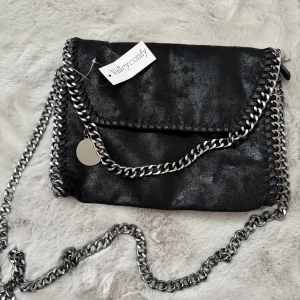 Svart axelväska med kedja - Supersnygg svart axelväska med kedjor längs kanterna och som axelrem. Väskan har magnetknäppning och innerfack med dragkedja. 💓Aldrig använd, lapp kvar!