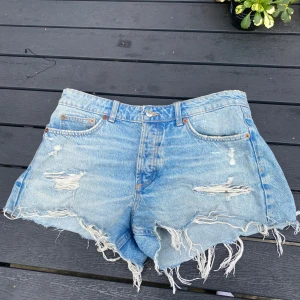 Blå jeansshorts med fransar från Zara - Snygga ljusblå jeansshorts från Zara med hög midja och råa, fransiga kanter. Shortsen har slitna detaljer och klassiska fem fickor.