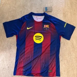 FC Barcelona Lewandowski matchtröja Nike - FC Barcelona hemmatröja med Lewandowski 9 på ryggen. Klassisk randig design i blått och vinrött med gula detaljer, klubbmärke och sponsorloggor. Tillverkad i lätt och ventilerande material, perfekt för fotbollsälskare.