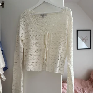 Vit spetskofta  - Säljer en söt vit kofta från Amisu med spetsmönster och knyt framtill. Koftan har v-ringad hals och långa ärmar, perfekt att slänga över en topp. Den är croppad och har fina detaljer i spetsen som ger en romantisk vibe.