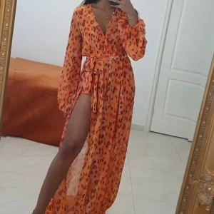 Orange långklänning med leopardmönster - Säljer en orange långklänning med leopardmönster och v-ringad hals. Klänningen har långa ärmar, slits och ett matchande bälte i midjan. Materialet är lätt och transparent, perfekt för att sticka ut med en cool vibe.