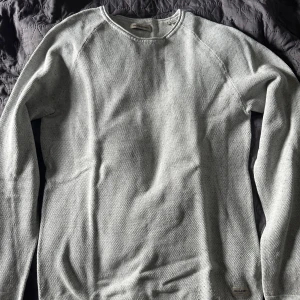 Ljusgrå stickad tröja Jack & Jones - En stilren ljusgrå stickad tröja från Jack & Jones i storlek S. Tröjan har rund halsringning och långa ärmar, perfekt för lager-på-lager. Materialet är mjukt och ger en clean look som funkar till jeans eller chinos. nypris 500kr