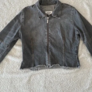Grå jeansjacka från Weekday - Snygg grå jeansjacka från Weekday med råa kanter och dragkedja framtill. Jackan har klassisk krage, långa ärmar med dragkedjor vid ärmslut och en croppad passform. Perfekt för dig som gillar en lite edgy stil.