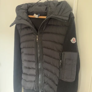 Svart Moncler pufferjacka med stickade ärmar - Snygg svart cardigan från moncler. Storlek S men kan även passa till storlek M. Är använd men fortfarande i väldigt bra skick. Säljer pågrund av att jag växt ur den