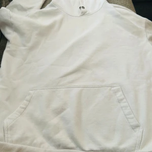 Vit hoodie från YOURTURN - Säljer en clean vit hoodie från YOURTURN med stor magficka och huva med metallöljetter. Tröjan har långa ärmar och ribbade muddar. Perfekt för chill dagar eller när du vill ha en enkel och snygg look. Materialet är mjuk bomull som känns skönt mot huden.