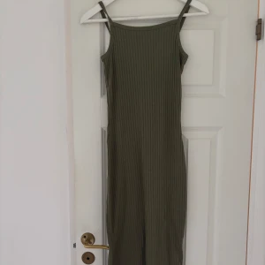 Olivgrön ribbad långklänning - Säljer en olivgrön långklänning med smala axelband och ribbad struktur. Klänningen är ärmlös och har en rak, slim passform som sitter snyggt mot kroppen. Perfekt för dig som gillar enkel och stilren design med lite edge. 