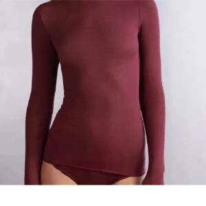 Vinröd intimissimi  - Snygg vinröd polotröja med lång ärm och tight passform. Tröjan är enkel och stilren utan detaljer, perfekt att matcha med jeans eller kjol. Materialet känns mjukt och följsamt mot kroppen, vilket gör den skön att bära hela dagen.