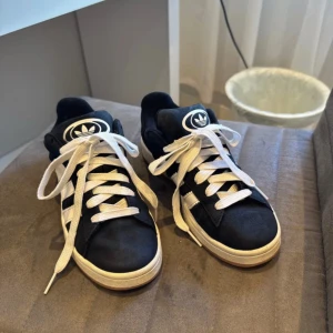 Adidas Campus sneakers svart/vit - Snygga Adidas Campus sneakers i svart mocka med klassiska vita ränder och vit sula. Skorna har rund tå, platt sula och vita snören. 