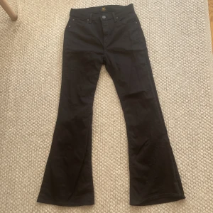 Svarta bootcut jeans från Lee - Snygga svarta jeans från Lee med klassisk femficksmodell och bootcut-ben. Jeansen har normal midja och är tillverkade i ett mjukt bomullstyg med lite stretch. Perfekta för dig som gillar en retroinspirerad look med utsvängda ben.