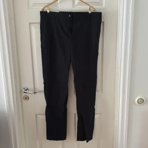 Svarta kostymbyxor från H&M - Svarta kostymbyxor från H&M med slim fit-passform. Byxorna har bälteshällor, två bakfickor med knappar och klassisk rak design. Perfekta för en clean och stilren look. Materialet är mjukt och följsamt, vilket gör dem bekväma hela dagen.