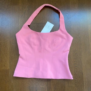 Rosa korsettopp från Zara - Supersnygg rosa korsettopp från Zara med breda axelband och markerade sömmar framtill. Toppen har en figurnära passform och är tillverkad i ett slätt, stadigt material som ger en riktigt clean look. Perfekt att styla med jeans eller kjol för en trendig vibe.