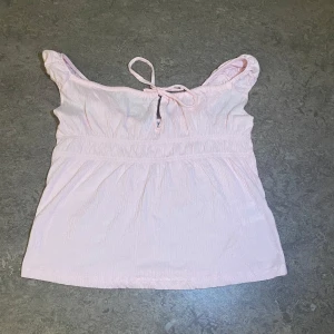 Ljusrosa linnetopp med knytband - Supersöt ljusrosa linnetopp med rynkade axelband och knytning framtill. Toppen har en luftig och lätt struktur, perfekt för varma dagar. den är aldrig använd