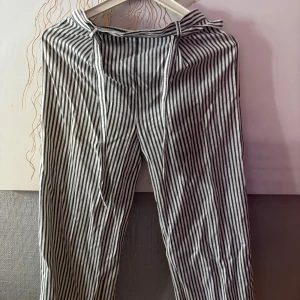 Randiga byxor med knyt från iDO - Snygga svartvita randiga byxor från iDO i storlek 164 Byxorna har elastisk midja och knytband framtill för extra stilpoäng. Tillverkade i mjuk polyesterblandning och har raka, lite loose ben. Perfekta för en chill och trendig look.