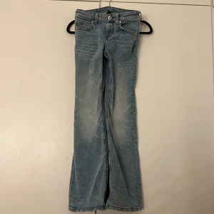 Ljusblå bootcut jeans med fickdetaljer - Snygga ljusblå jeans med bootcut passform och coola fickor med lock och knapp framtill. Jeansen har klassisk femficksdesign, bälteshällor och är tillverkade i mjukt denim. Perfekta för dig som gillar en avslappnad men trendig look.