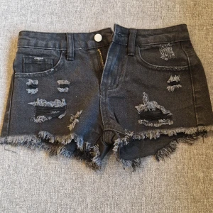 Svarta jeansshorts med slitningar - Säljer ett par svarta jeansshorts feån Shein med fransiga kanter och slitna detaljer framtill. Köpte den för ett tag sedan och har inte kommit till andvändning någon gång. 