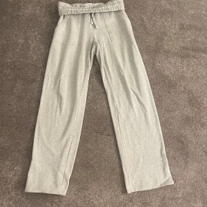 Grå mjukisbyxor med snörning - Snygga ljusgrå mjukisbyxor med bred resår och snörning i midjan. Byxorna har raka ben och två fickor framtill. Perfekta för chill dagar eller när du vill vara extra bekväm.