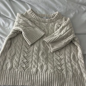 Beige stickad tröja från Zara - Säljer en beige stickad tröja från Zara i storlek S. Tröjan har ett snyggt flätmönster och breda ribbade muddar vid ärmslut och nederkant. Rund halsringning och långärmad modell, perfekt för att hålla sig varm under kyliga dagar.