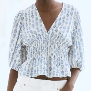 Vit och blå blommig blus  - 🔔LAPP FORTFARANDE PÅ🔔Supersöt blus i vit med blått blommönster, croppad passform och v-ringad hals. Blusen har puffiga trekvartsärmar och snygg rynkning i midjan som ger en cool siluett. Perfekt för dig som gillar romantiska detaljer och fräsch stil. Helt ny 