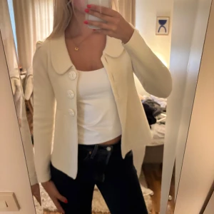 Vit cardigan jacka med stora knappar - Superfin vit cardigan jacka med stora dekorativa knappar och bred krage. Jackan har en figurnära passform. H&M vintage.