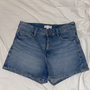 Blå jeansshorts från H&M - Klassiska blå jeansshorts från H&M i modell med normal passform och fyra fickor. Shortsen har bälteshällor, knapp och dragkedja framtill samt raka ben. Perfekta för sommaren och enkla att matcha med allt.