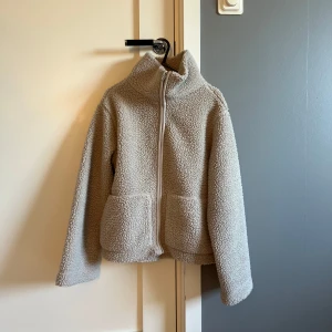Beige teddyjacka lager 157 - Mysig beige teddyjacka från lager 157 i storlek XS. Jackan har hög krage som kan vikas ner, två stora fickor framtill och stängs med dragkedja!